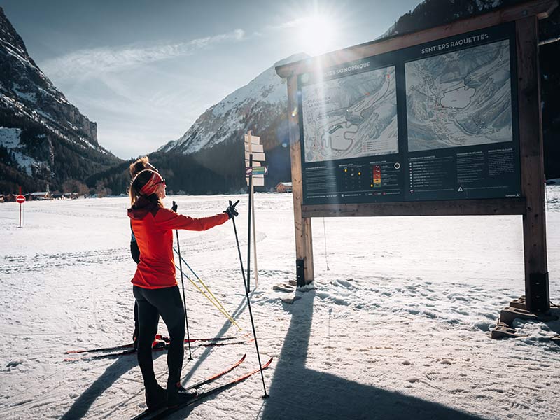 une femme et un homme en ski de fond qui regardent le plan des pistes sous le soleil - © Simon Morice